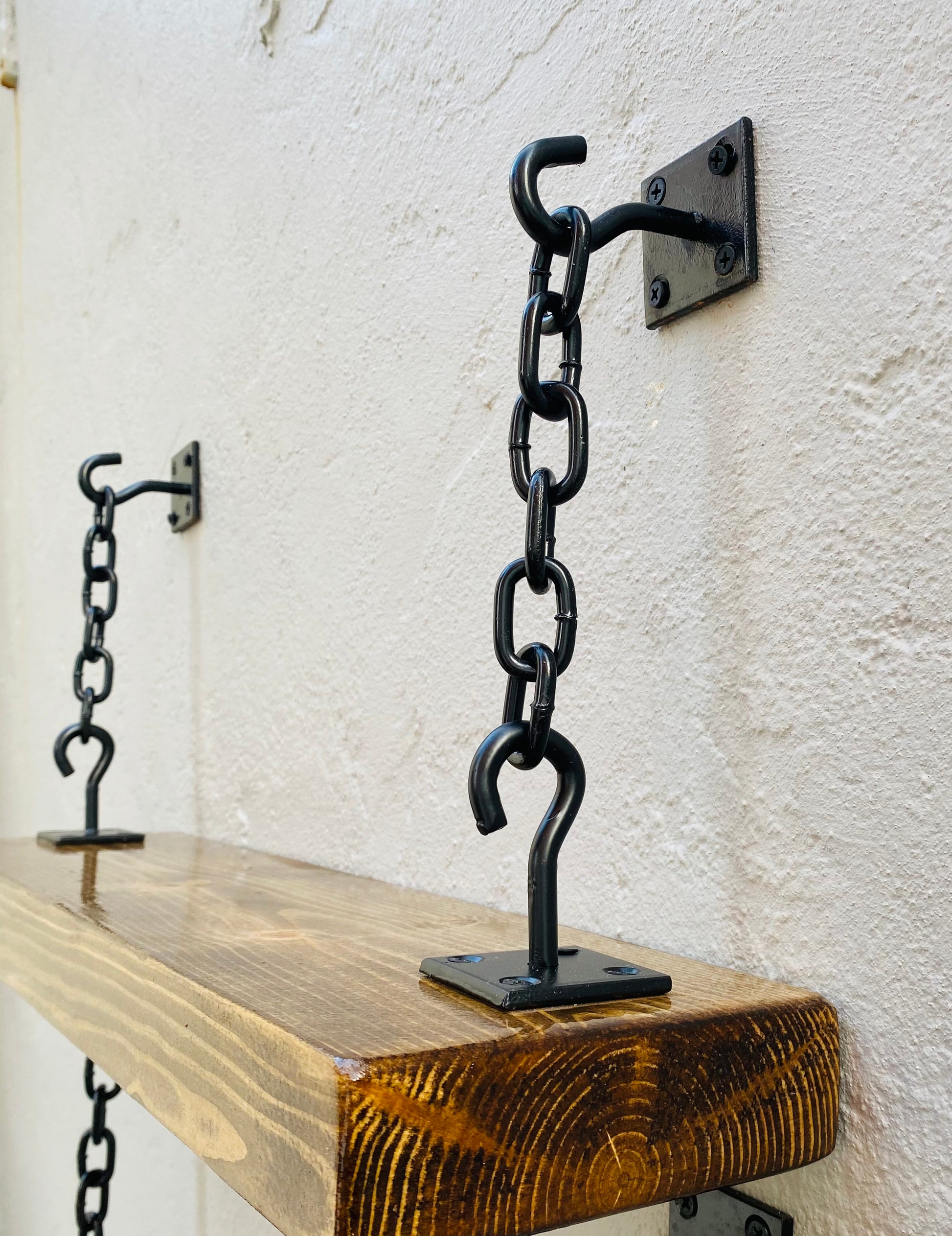 Black hook and chain shelf brackets attached to a wood shelf wall mounted